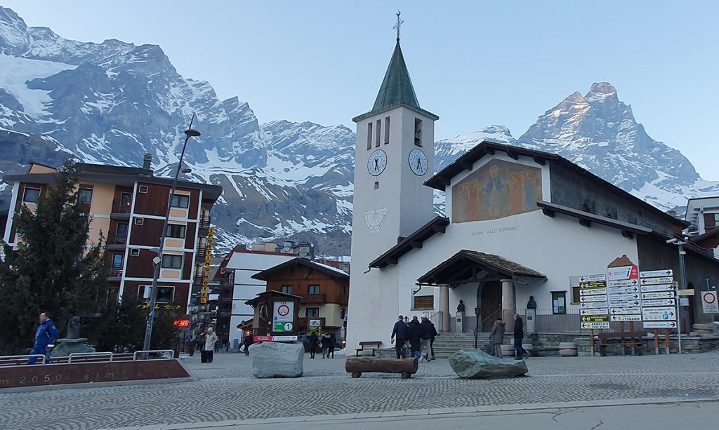 Kirkko sijaitsee Cervinian kylän keskustassa. Taustalla näkyy vuoria