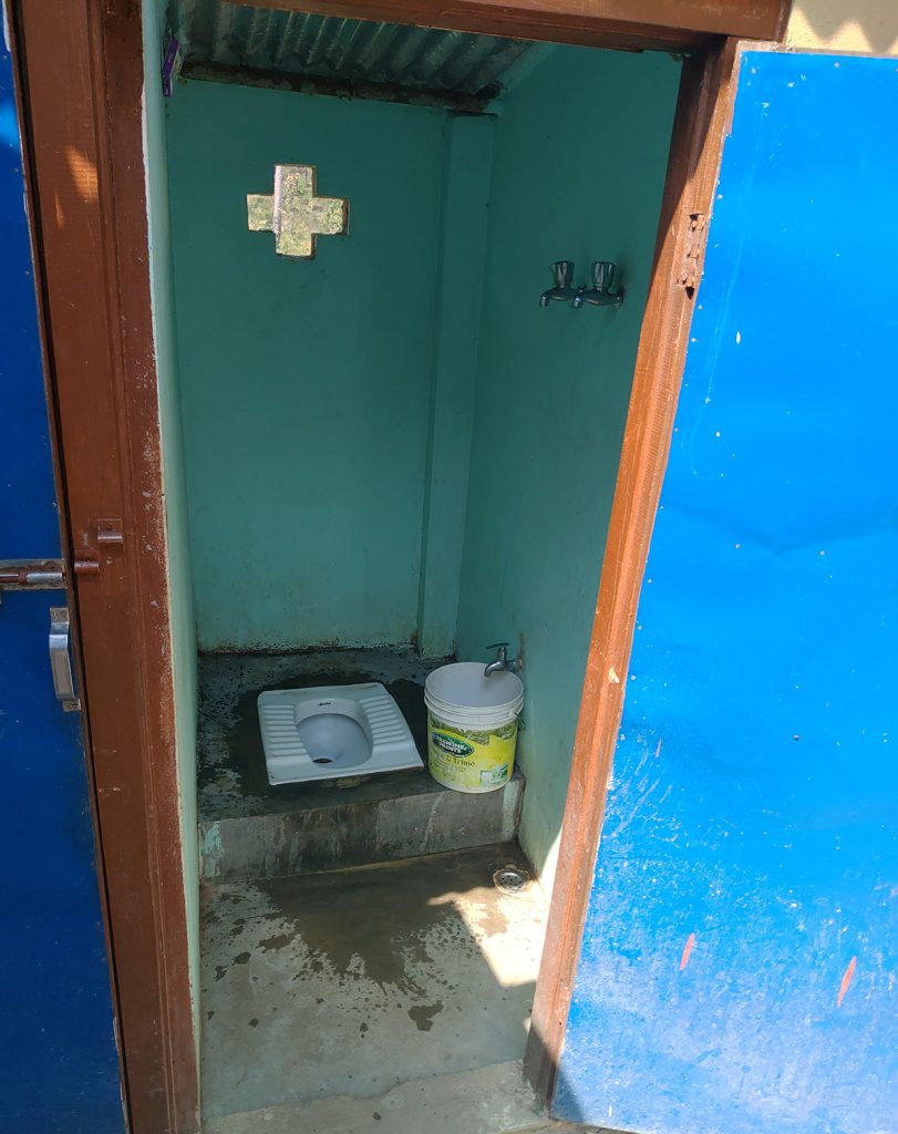 Alkeellinen käymälä, jossa reikä lattiassa ja vesihana seinässä