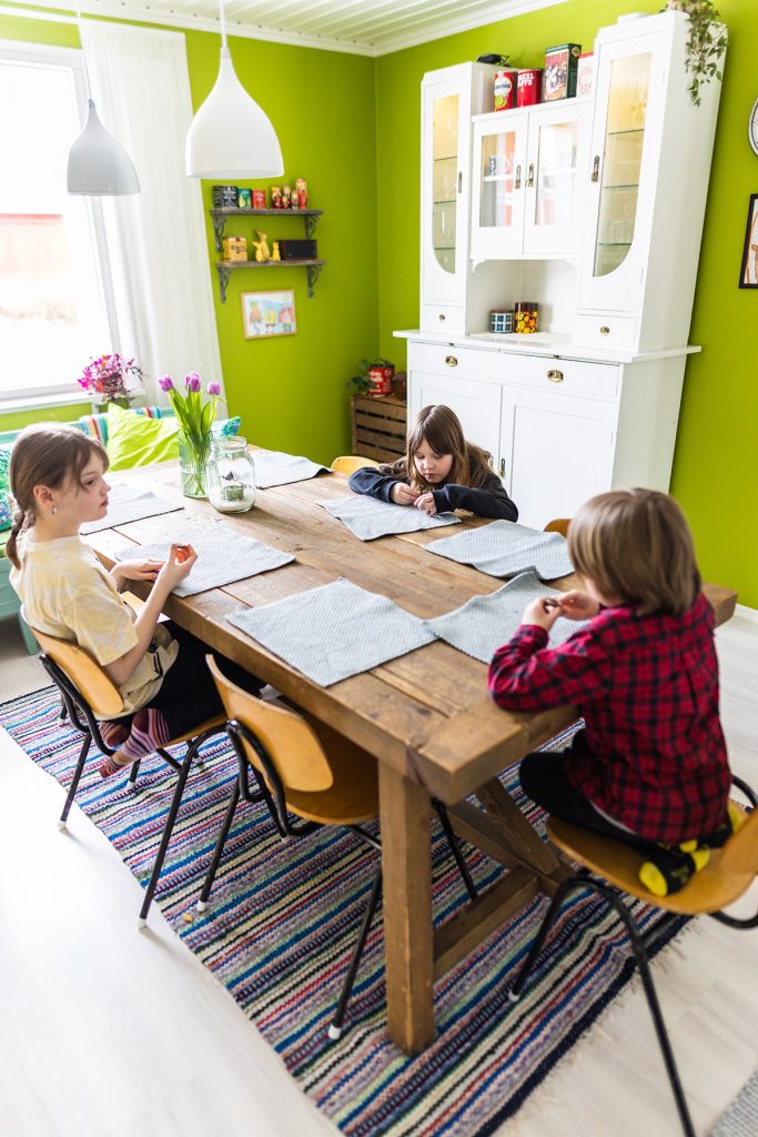 Kolme lasta istuvat keittiössä pöydän ympärillä ja syövät välipalaa